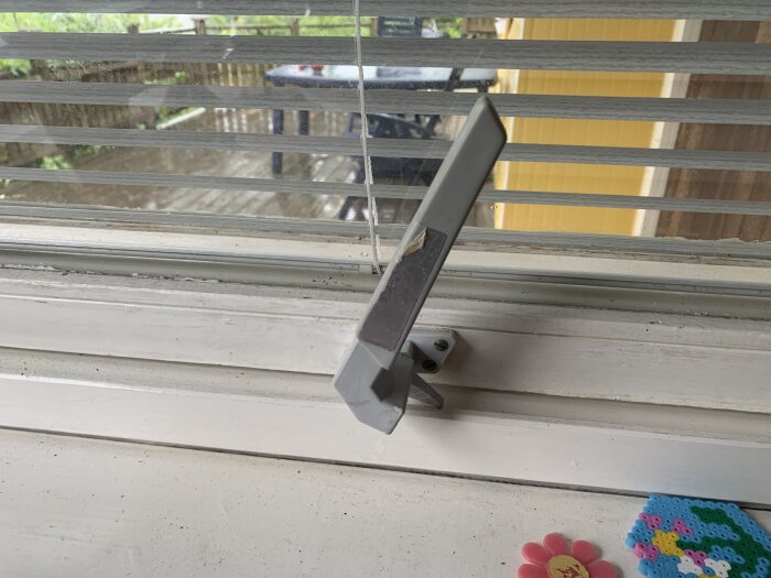 Trasigt fönsterhandtag med synliga persienner och träveranda utanför.
