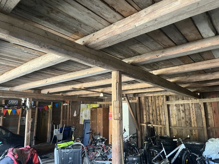 Loftliknande utrymme med trästolpar och bjälkar i ett garage med cyklar och färgglada vimplar.
