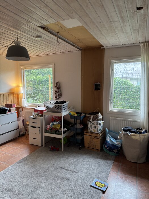 Rum med oavslutad renovering, tillfälligt möblerat med lådor och kassar. En matta döljer golvets tidigare köksöns hål.