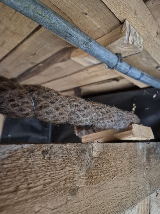 Flätad materialtätning runt rör i träkonstruktion.