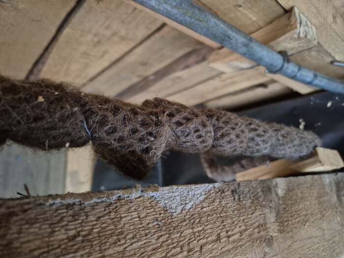 Brun, fiberrik isolering eller material under ett trätak med ett rör intill; fråga om det är asbest eller talg.