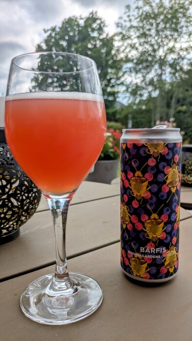 Ett glas med suröl från Småland och en färgglad burk med texten "BARFIS Kvarnagårdens Bryggeri" på ett bord utomhus.
