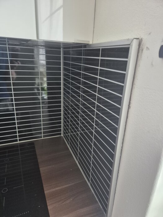 Svart och vitt kakelstänkskydd i kök, delvis löst från väggen, med angränsande bänkskiva och spishäll.