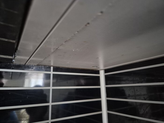 Närbild på ett köksstänkskydd, svartvita plattor, delvis avlägsnat och fastlimmat, monterat vid en vägg i en lägenhet.