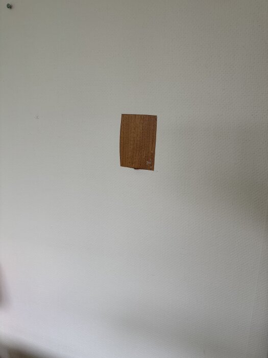 Vit vägg med ett litet fyrkantigt hål där en träplatta tidigare suttit.
