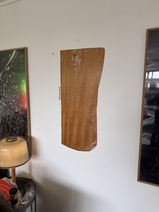 Träskiva avslöjar igenmurad dörr i en vägg, omgiven av tavlor och en lampa med dekorationer på ett bord i förgrunden.