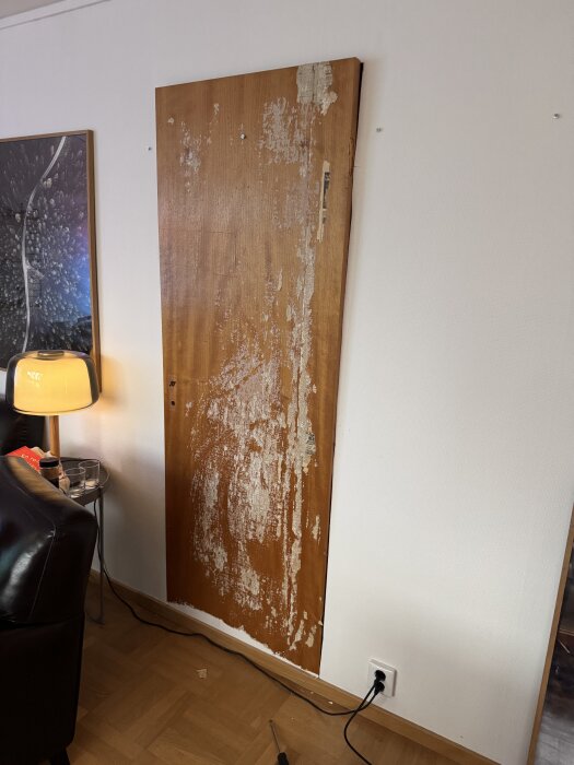 En dold dörr med bortskrapad färg syns bredvid en tavla och lampa; dörren har bevarats bakom väggen.