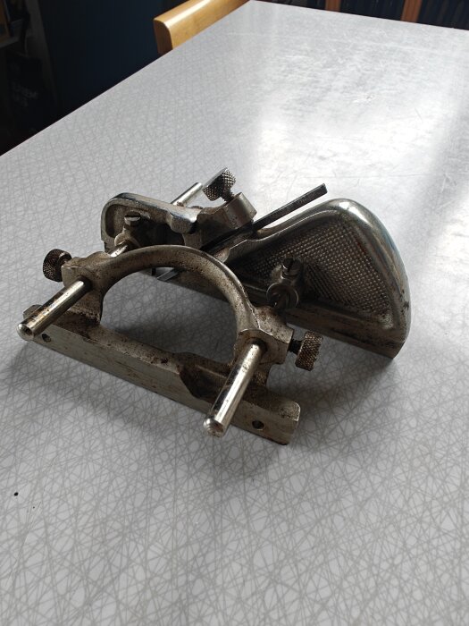 Metallisk handhållen skärande verktyg liggande på ett vitmönstrat bord.