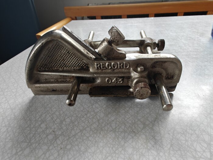 En metallisk Record 043 hyvel på ett bord, använd i lek om blocket-fynd, med detaljerade skruvar och handtag.