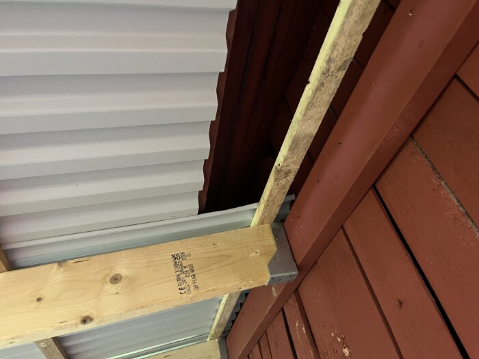 En vriden träregel och överlappande plåtprofiler på ett bygge, där plåten verkar vara för hög och tar i fotbrädan.