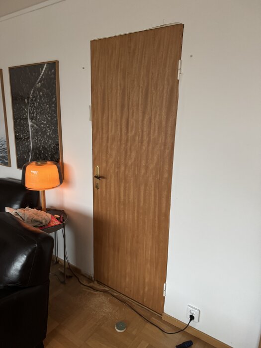 Trädörr utan lister installerad i ett rum, med en orange lampa bredvid, kopplade kablar och några verktyg på golvet. Temporär lösning.