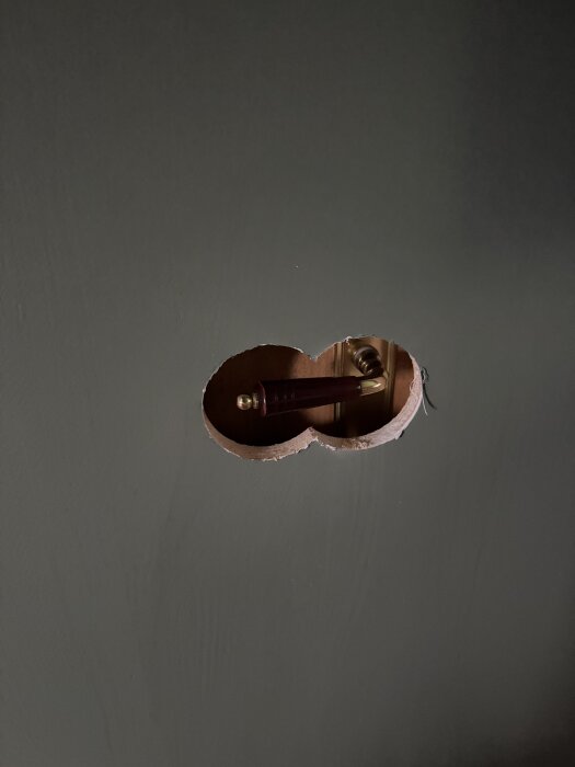 Hål i grå vägg med mörkt dörrhandtag och karm synliga inuti.