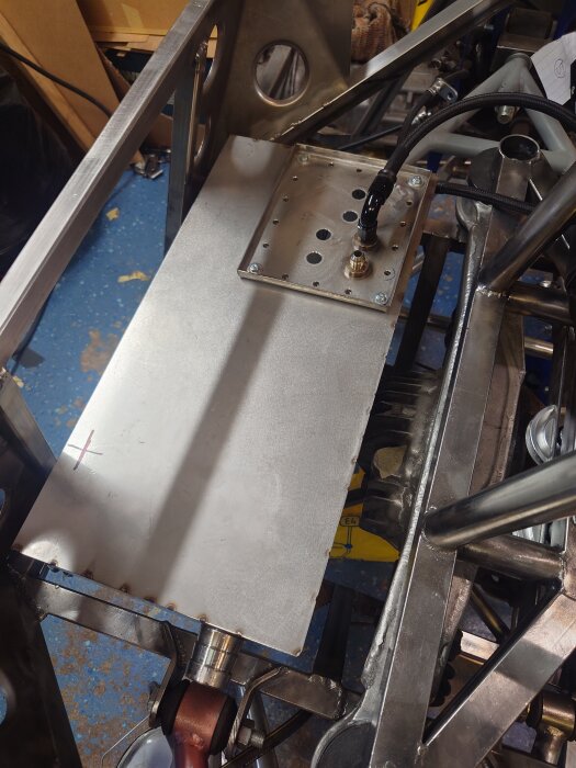 Metalltank inuti en konstruktion med en slät yta och anslutningsdetaljer. En rörkoppling och svetsfogar syns.