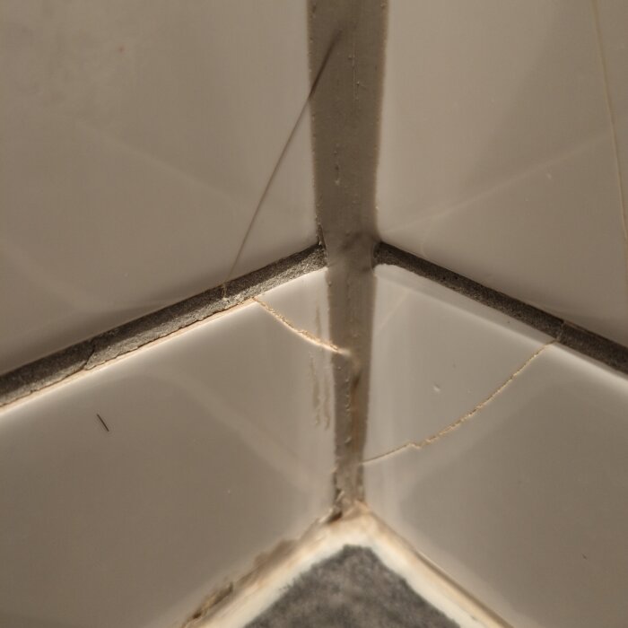 Sprickor i badrumskakel vid ett hörn, med synliga fogar och små skador på plattorna.