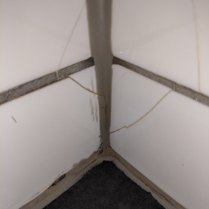 Sprickor i kakel och fog i ett badrumshörn.