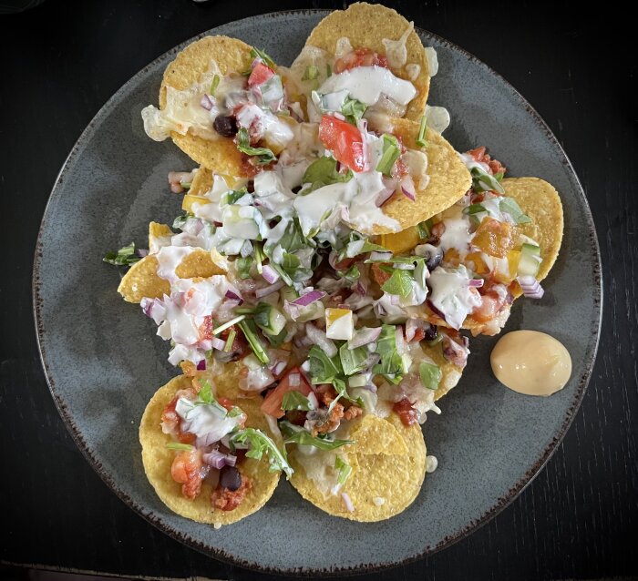 Tallrik med nachos toppade med sallad, salsa, vitlökssås och rester från chili con carne, med dressing vid sidan.