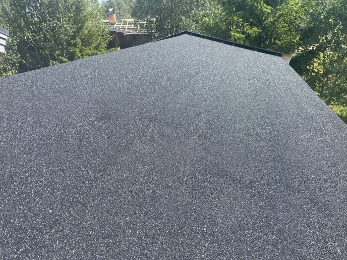 Nybyggt svart tak med färdig yta. Omgivande träd syns i bakgrunden.