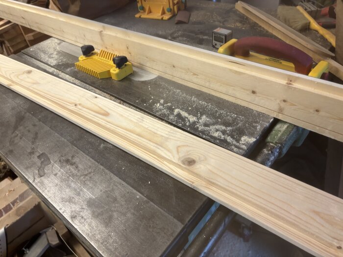 Träplankor på arbetsyta med justersåg och fingerboard i verkstadsmiljö.