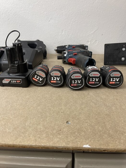 Bilden visar flera Bosch 12V Li-ion-batterier och laddare upplagda på en hylla, samt två borrmaskiner i bakgrunden.