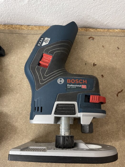 Bosch GKF 12V-8 kantfräs visas liggande på träbord, används för precisa snickeriarbeten. Framgångsrik i sin kompakta design och ergonomiska handtag.