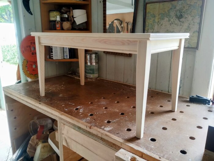 En nybyggd träbänk av överblivet virke står på ett arbetsbord i snickarverkstad, redo för målning med linoljefärg.