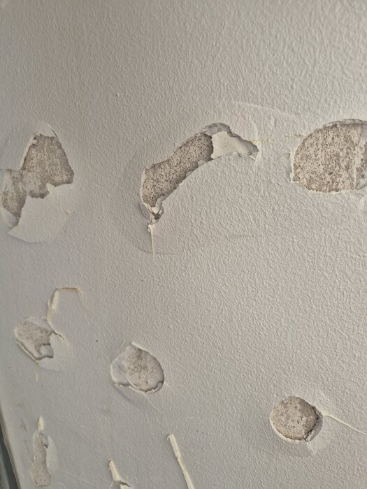 Vägg med flera fläckar där färg och puts har lossnat, vilket avslöjar underliggande yta.