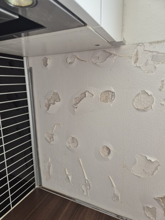 Vägg med avskalat färg och skador under köksskåp, med synliga märken och ojämn yta.