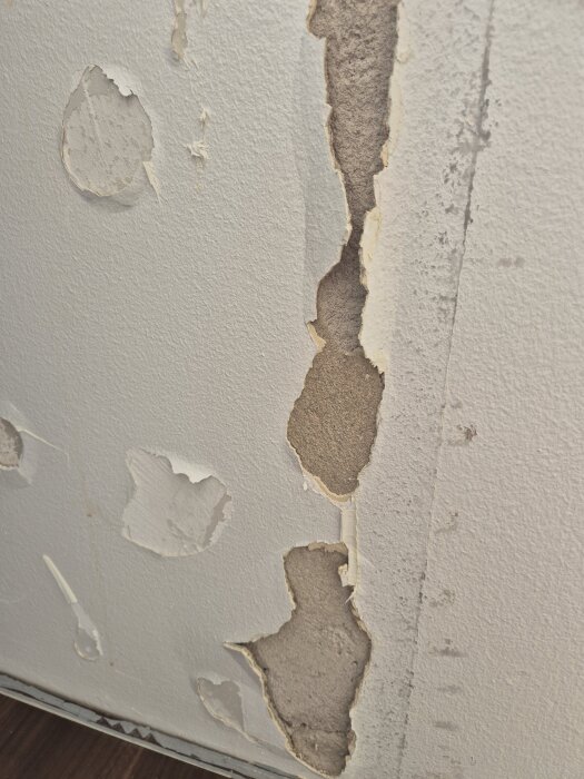 Skadad vägg med flagande färg och synligt underlag, visar behov av renovering.