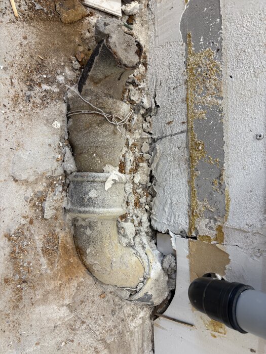 Stort rör synligt i köksgolvet efter borttagning av skåp och golv; rör omgiven av smuts och brottytor, fråga ställd om rörens funktion.