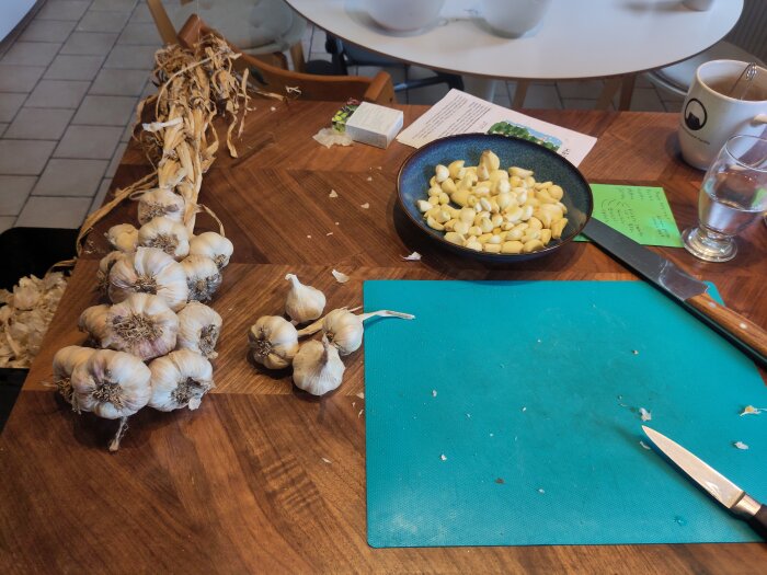 Vitlöksknippen och skalade klyftor på ett köksbord, med en kniv och skärbräda i förgrunden, förbereder för torkning och pulver.