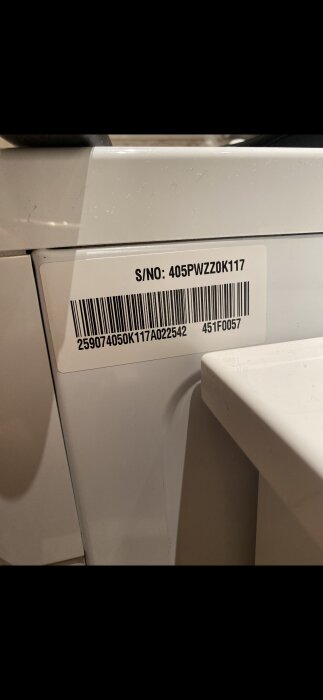 Vit tvättmaskin med klistermärke som visar serienummer "405PWZZ0K117" och streckkod samt andra nummer.