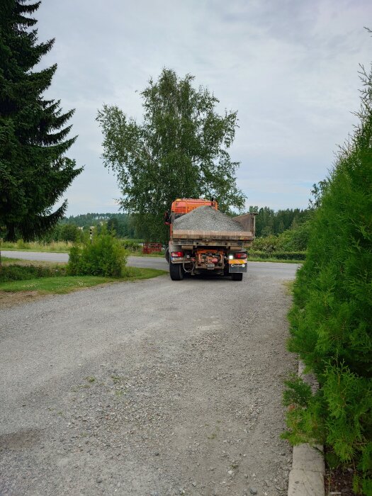 En grusväg med en lastbil fylld med grus, omgiven av träd och grönska.