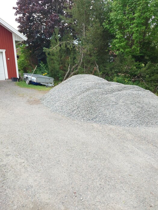 Grushög på uppfart bredvid ett rött hus och en släpvagn, omgiven av gröna träd.