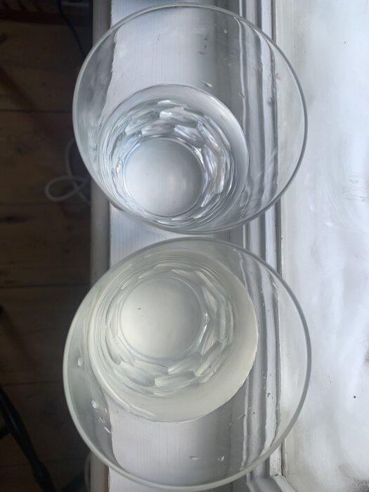 Två glas med vatten, ett klart från kommunen och ett grumligare från en grävd brunn, jämförs för färgskillnad på ett fönsterbräde.