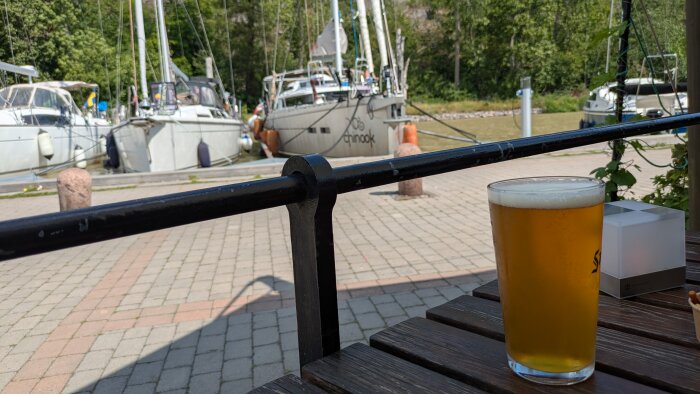 Ett glas öl på ett bord utomhus, med segelbåtar förtöjda vid en kanal i bakgrunden.