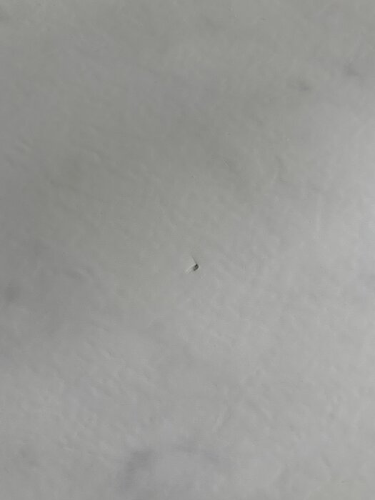 Hål i grå våtrumsmatta i tvättstuga nära en oanvänd dusch.