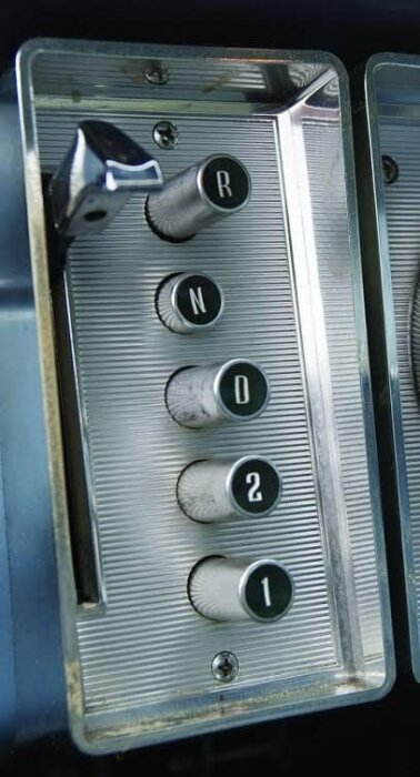 Växelpanel från en äldre amerikansk bil med knappar märkta R, N, D, 2 och 1 i en vertikal rad, inramat i metall.