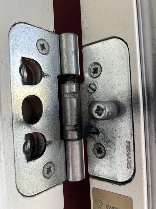 Gångjärn på ytterdörr med stjärnskruvar, märkt med "FSKARS", monterat på en vit och röd dörr.