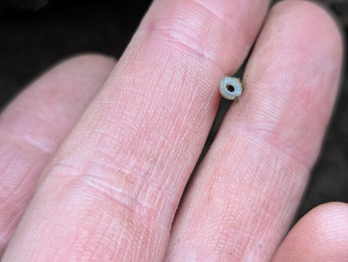 Närbild på en hand som håller i ett litet, avskuret rör eller kabelbit.