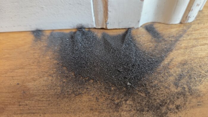 Svart damm eller sandliknande material på golvet vid vit golvlist i ett nyligen renoverat rum.