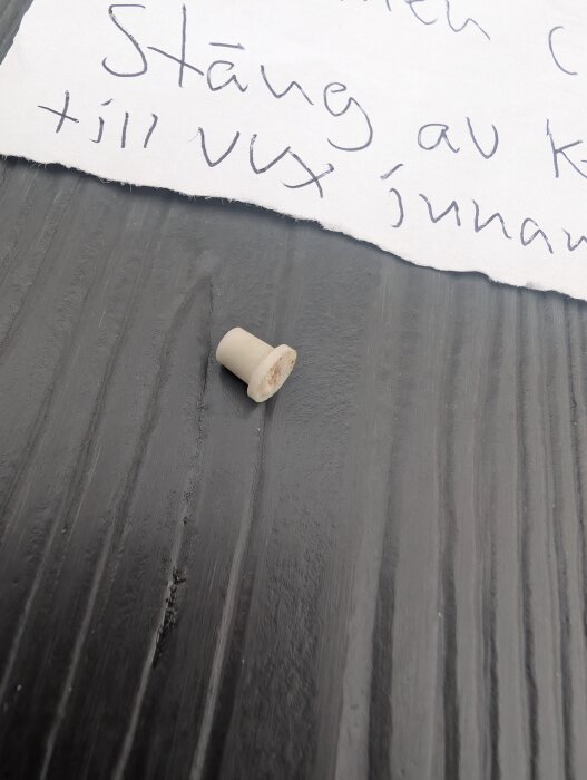 Liten hylsa på ett mörkt bord bredvid en handskriven lapp.