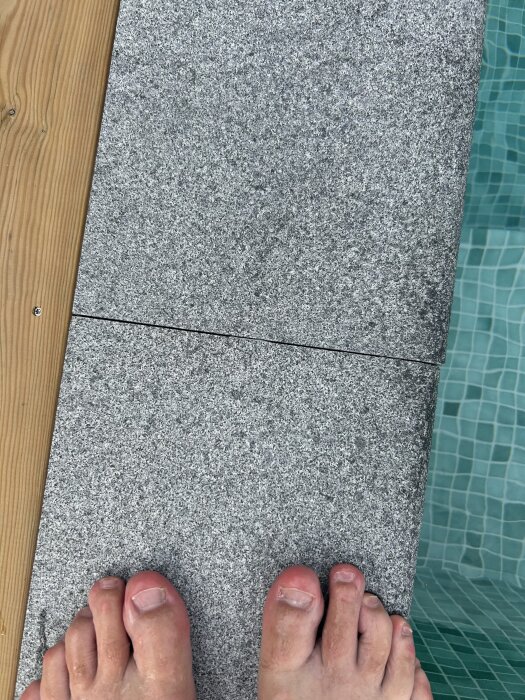 Grå stenplattor intill en pool med träkant och några tår synliga, visar mellanrum mellan plattorna.