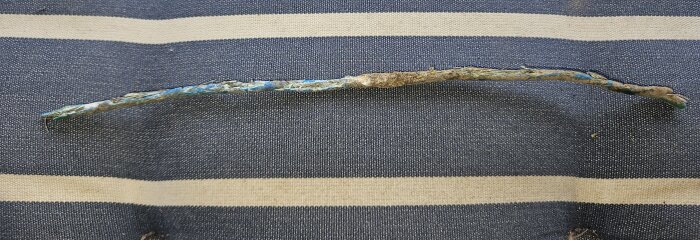 En gammal, delvis korroderad kabel ligger på ett tygunderlag. Kabeln har synliga skador och missfärgningar.