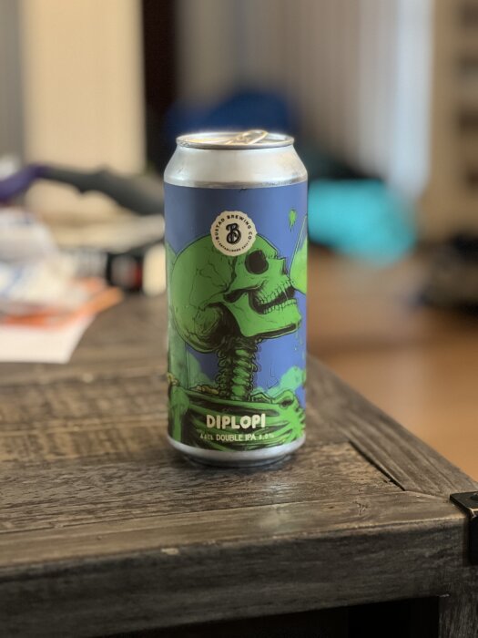 Ölburk av Bustad Brewing Co med konstverk av en grön dödskalle på blå bakgrund, etiketten "DIPLOPI" framträdande.
