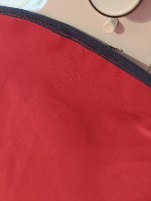 Röd tygbit med mörkblå kant, del av en handsydd påse för trangia, avigsidan utåt. Sömmen är synlig i bild.