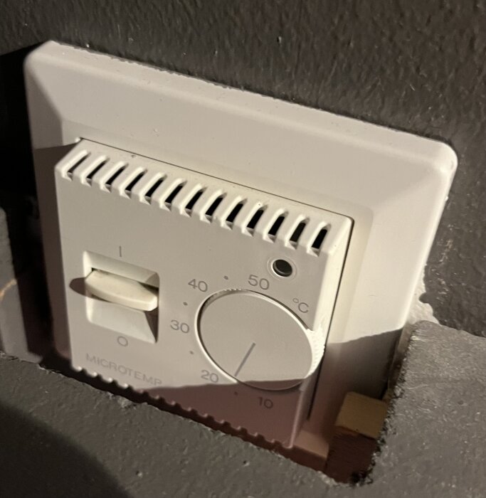 Väggmonterad termostat med vred för temperaturinställning, märkt "Microtemp", och switch för på/av-läge.