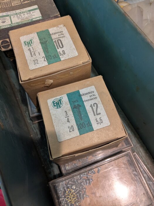 Lådor med träskruv av stål, etiketter visar specifikationer som storlek och antal. Finns i en blå metallbehållare.