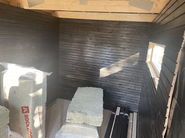 Isolerade väggar och färdig panel i ett rum med isoleringsmaterial från Rockwool staplat på golvet.