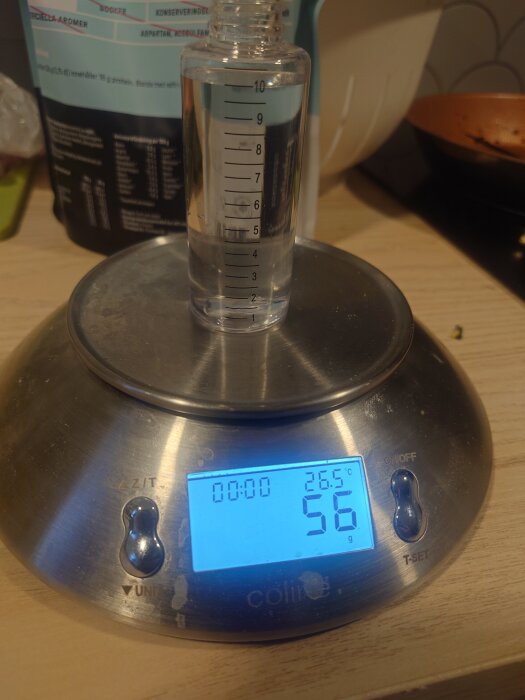 En flaska med vÀtska stÄr pÄ en digital köksvÄg, som visar 56 gram och 26,5 grader Celsius.
