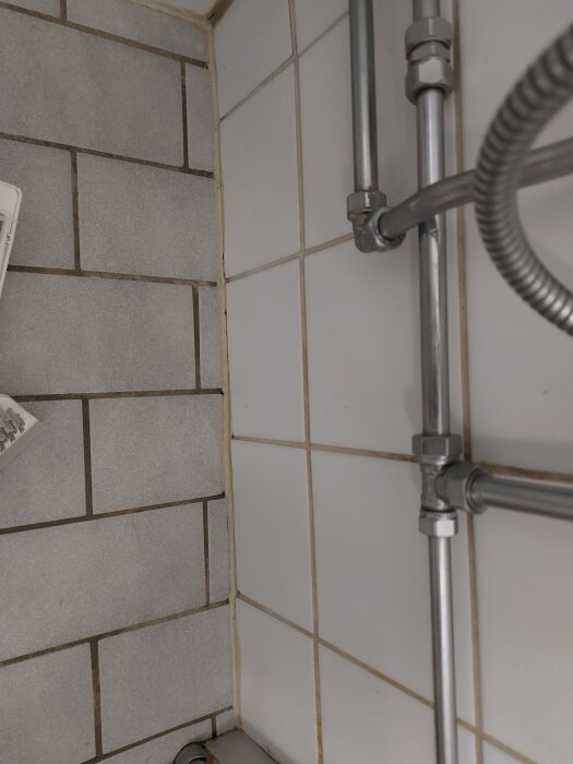 Badrumsvägg med vitt kakel, synlig spricka och mögel i fogarna intill metallrör.